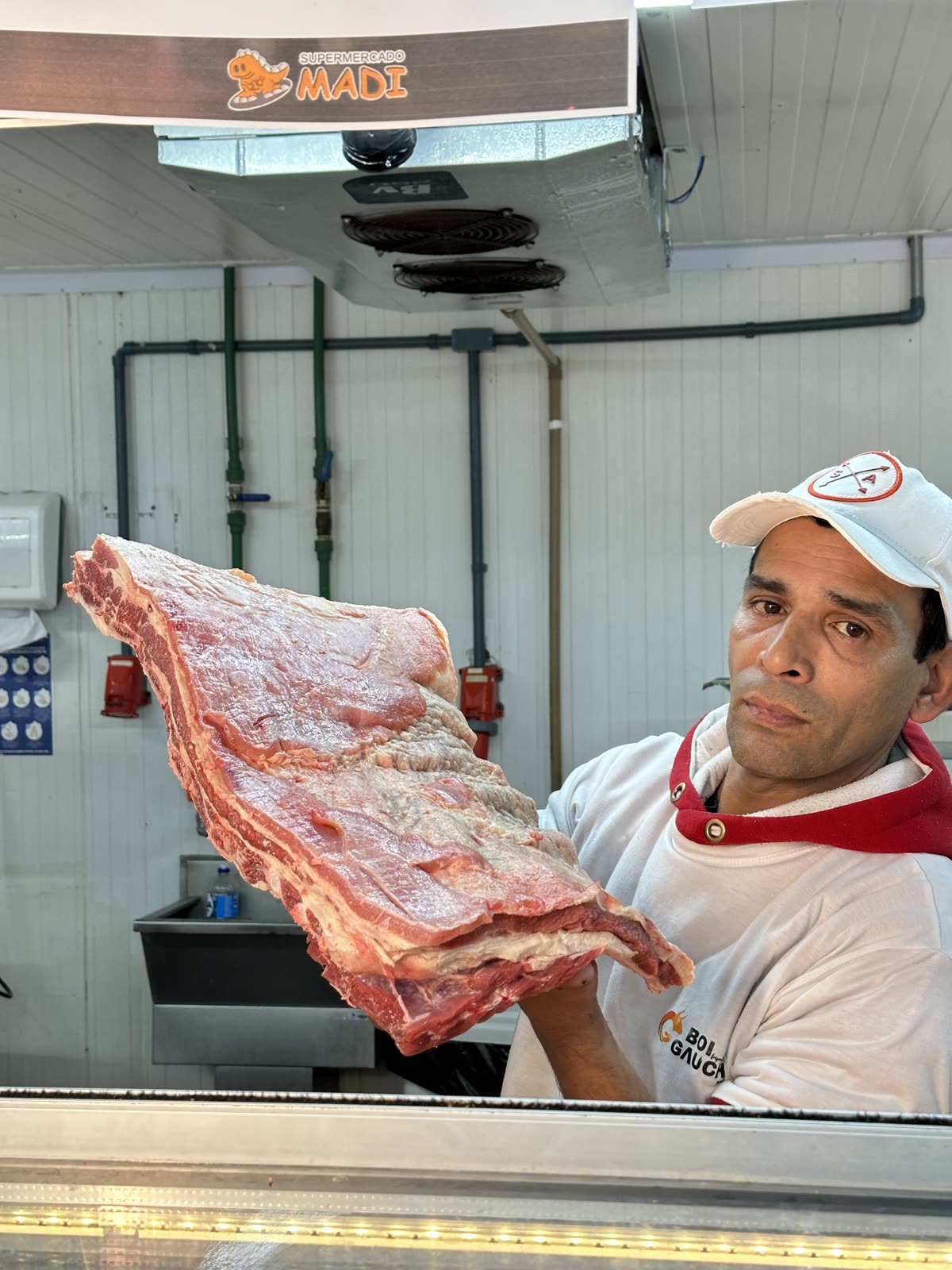 Profissional do açougue apresentando um corte de carne dentro do Supermercado Madi