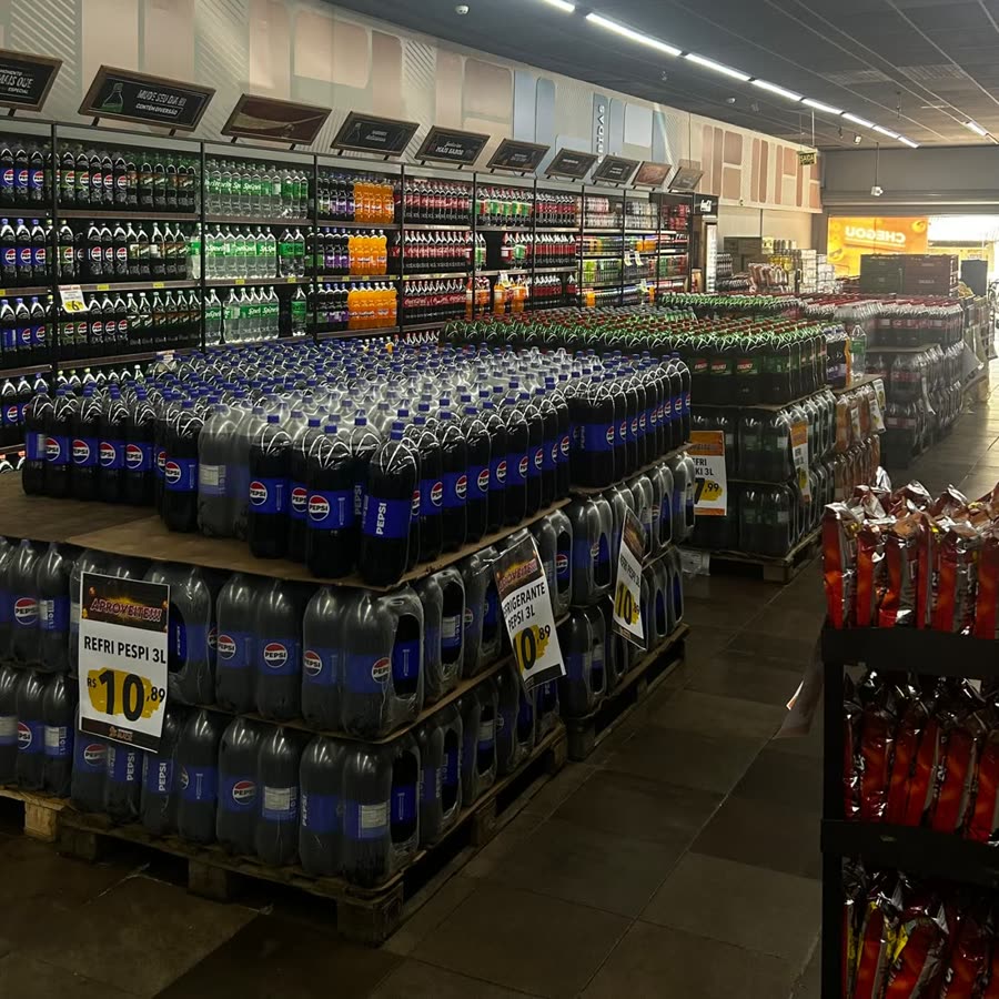 Setor de bebidas, com prateleiras altas de refrigerante e paletes no corredor