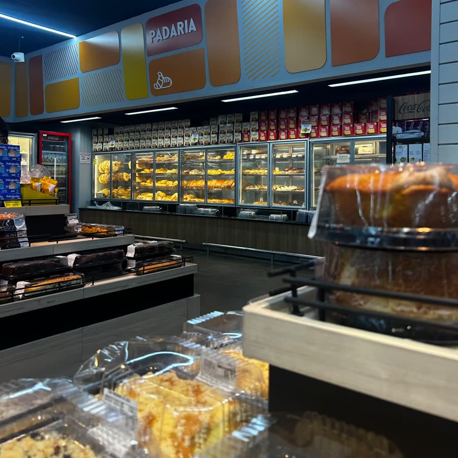 Vitrines da padaria cheias de pães e doces, sob o letreiro do setor